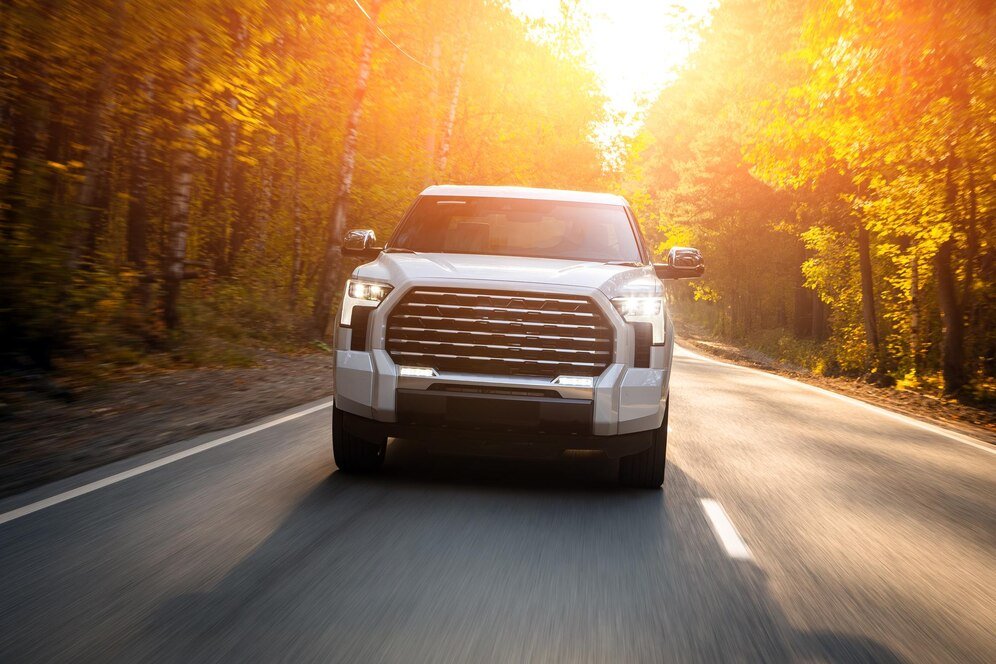 white-suv-driving-street-warm-day-against-backdrop-forest