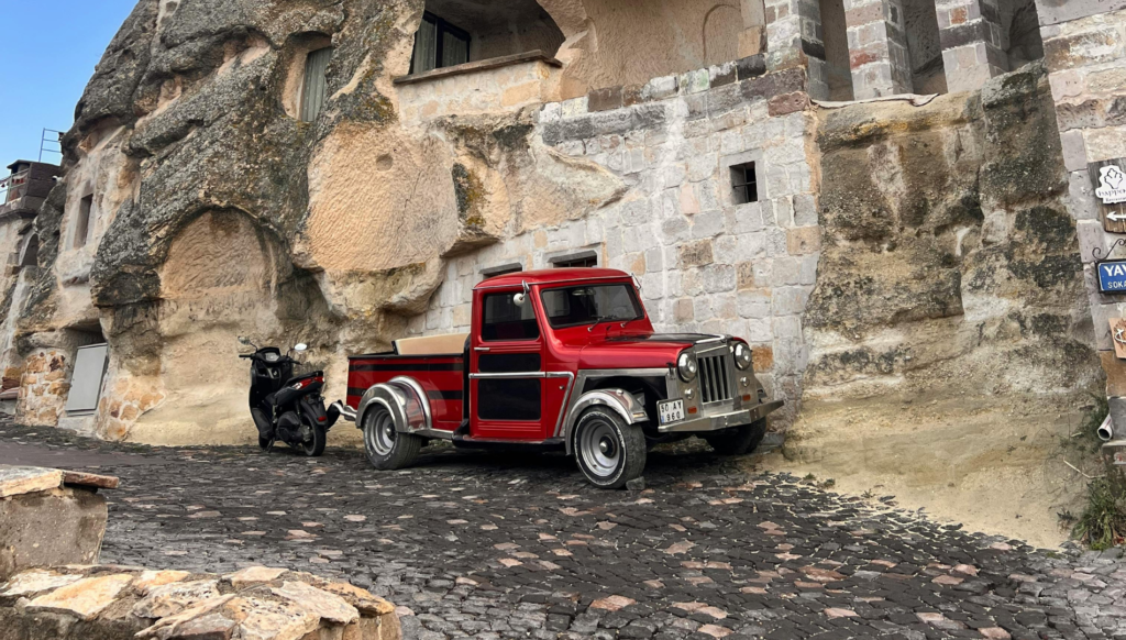Vintage red pickup truck parked on a cobblestone street near stone buildings.