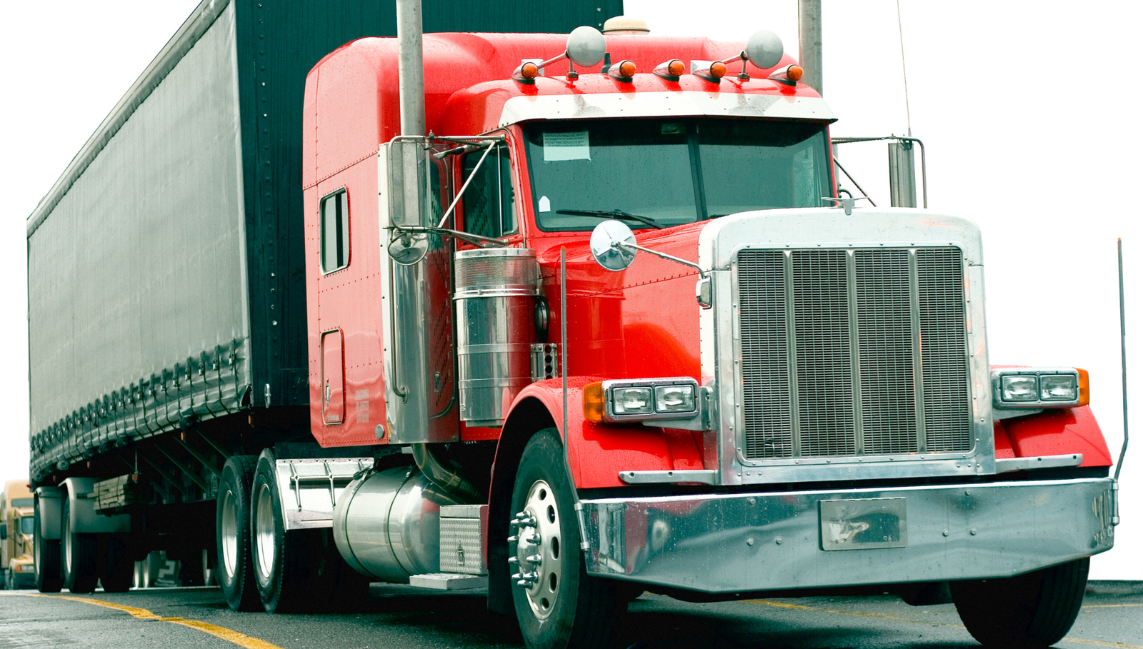 Red semi truck with trailer parked on a roadway.