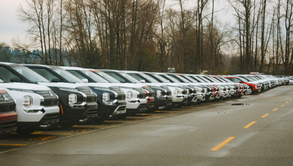 Row of new compact SUVs parked in a dealership lot on a cloudy day with bare trees in the background.
