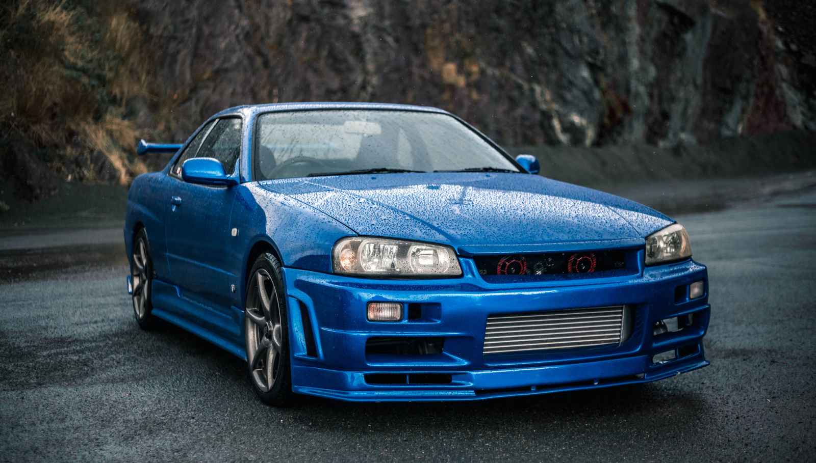 Blue sports coupe parked on a wet mountain road.