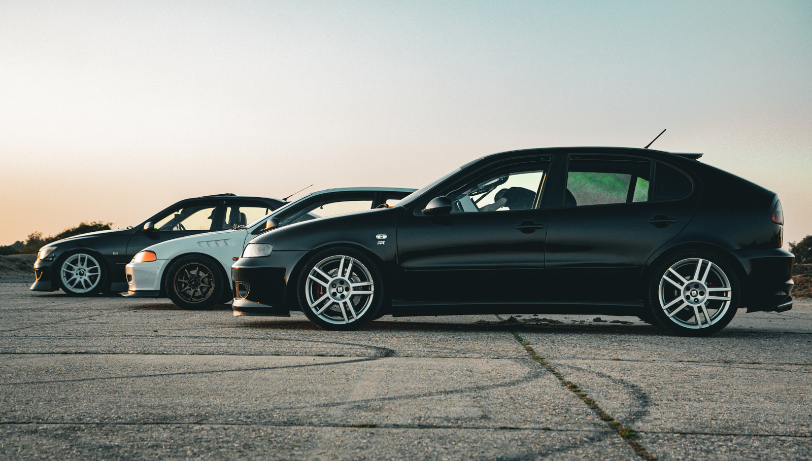 Three modified hatchback cars parked side by side outdoors.