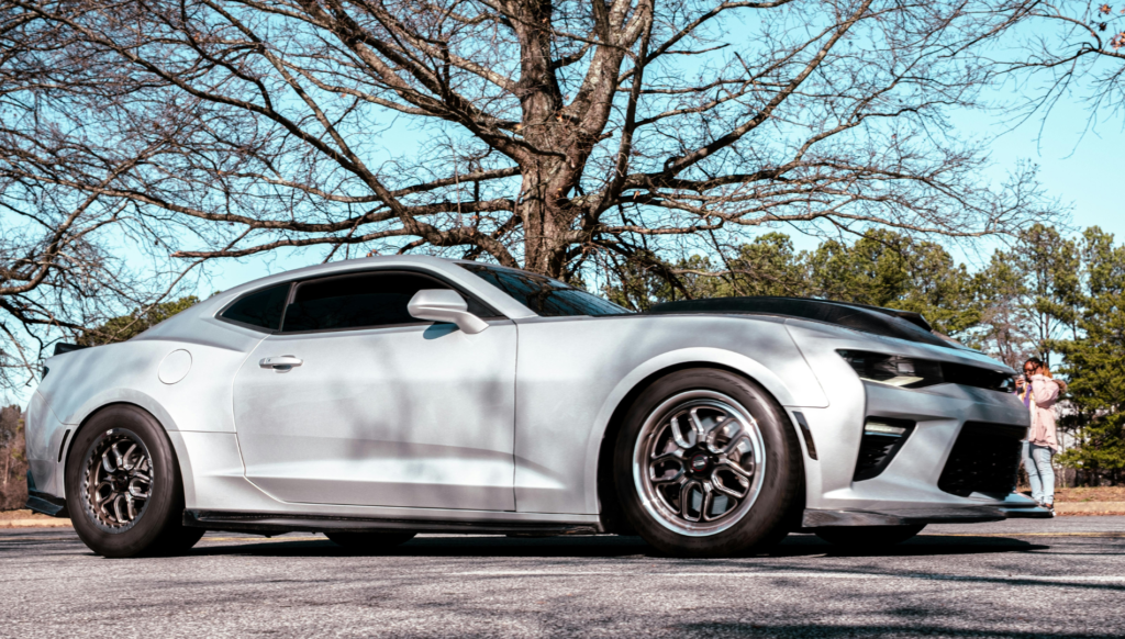 White sports coupe parked outdoors near trees.