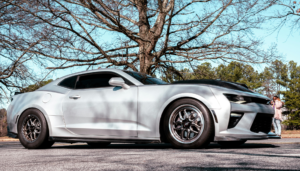 White sports coupe parked outdoors near trees.